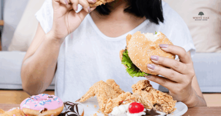 Person eating a burger, fried chicken, and sweets, symbolising eating disorders and co-occurring addiction treatment at White Oak Recovery Center