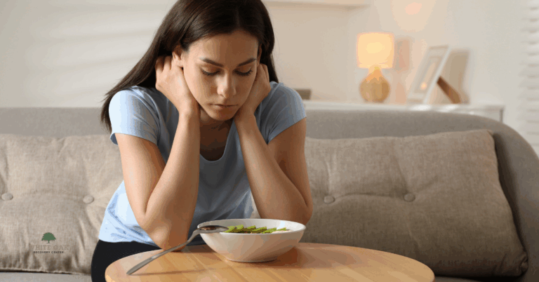 Young woman sitting on a sofa looking down at a bowl of food, representing rumination disorder and treatment support at White Oak Recovery Center